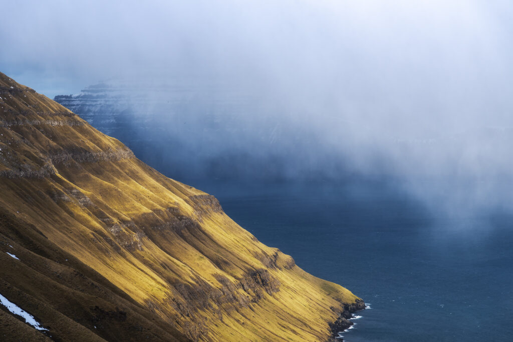 Sunlit grassy cliffs above a deep blue fjord, Faroe Islands